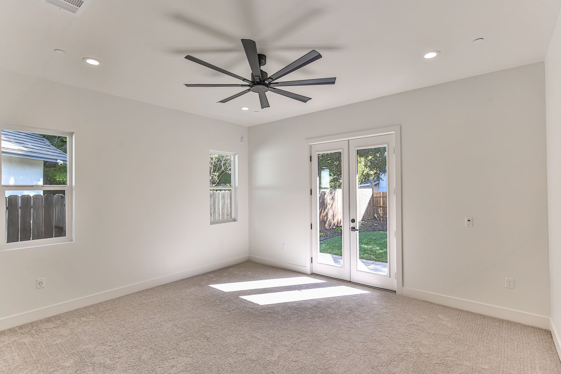 An empty room with a ceiling fan and sliding glass doors.