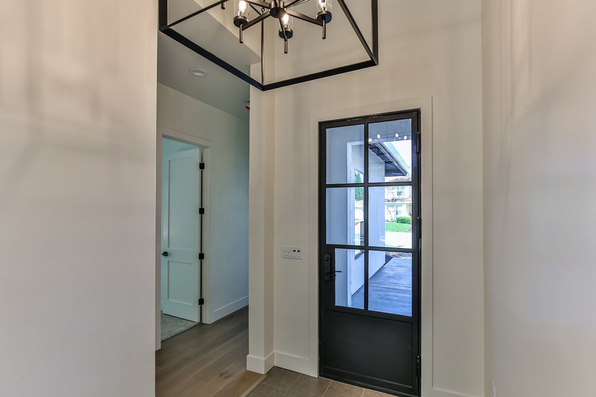 A hallway with a black door and a chandelier hanging from the ceiling.
