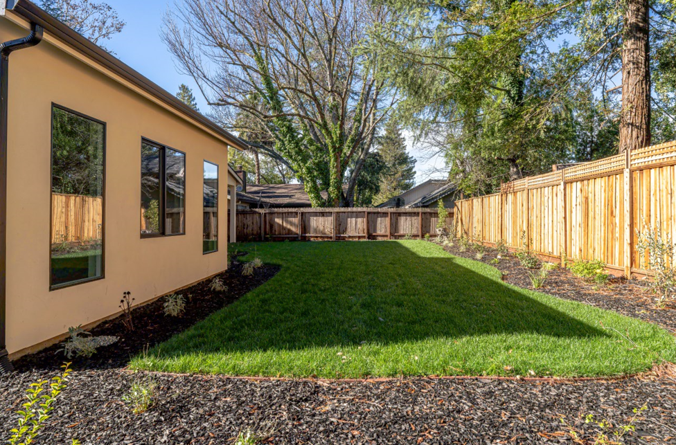 Backyard with green lawn, a tan house, and a wooden fence.