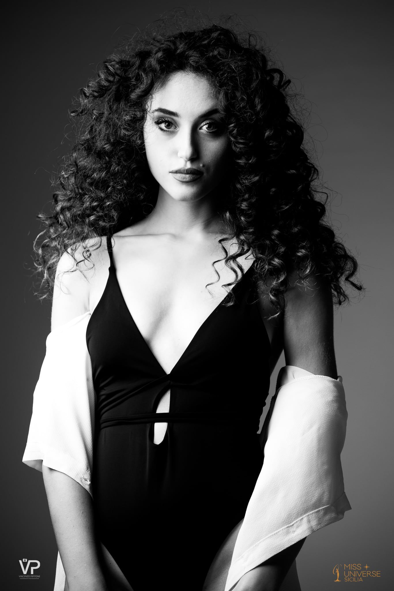 Una donna con i capelli ricci indossa un costume da bagno nero e un maglione bianco.