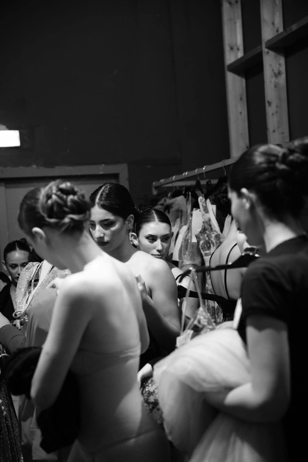 Un gruppo di donne è in piedi in una stanza con i vestiti appesi su degli attaccapanni.