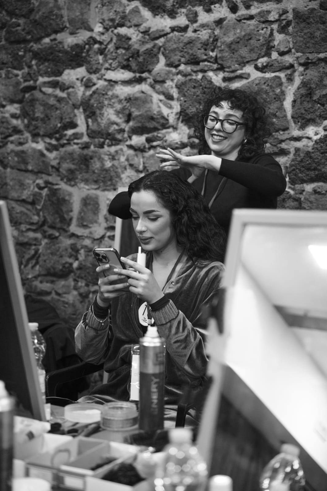 Una donna si sta facendo fare i capelli dal parrucchiere mentre guarda il telefono.