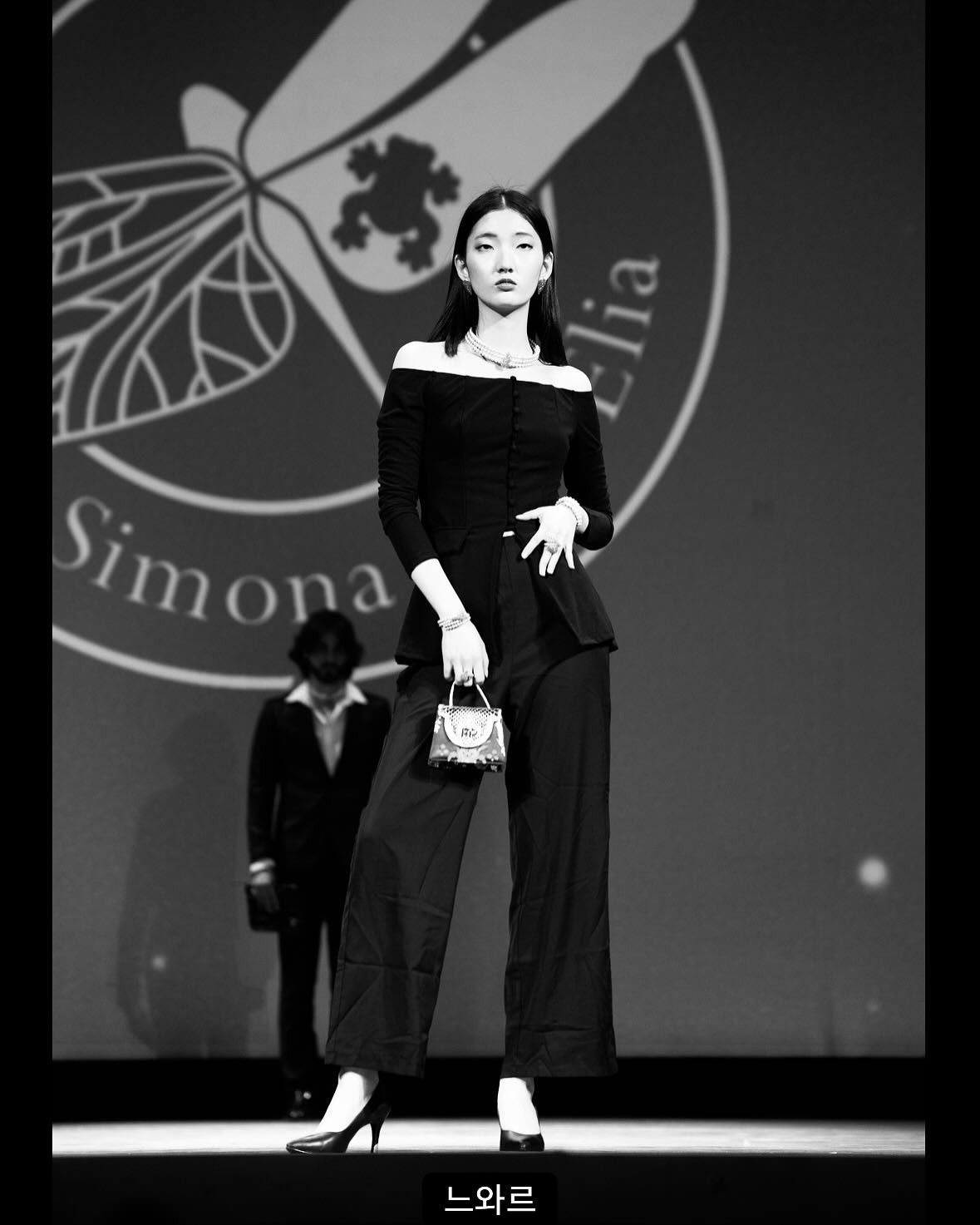 Una foto in bianco e nero di una donna in piedi davanti a un cartello con la scritta simona