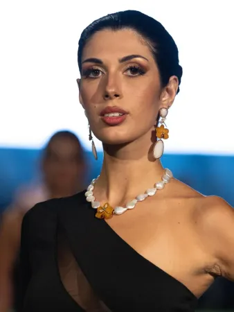 Una donna con i capelli ricci indossa un costume da bagno nero e un maglione bianco.