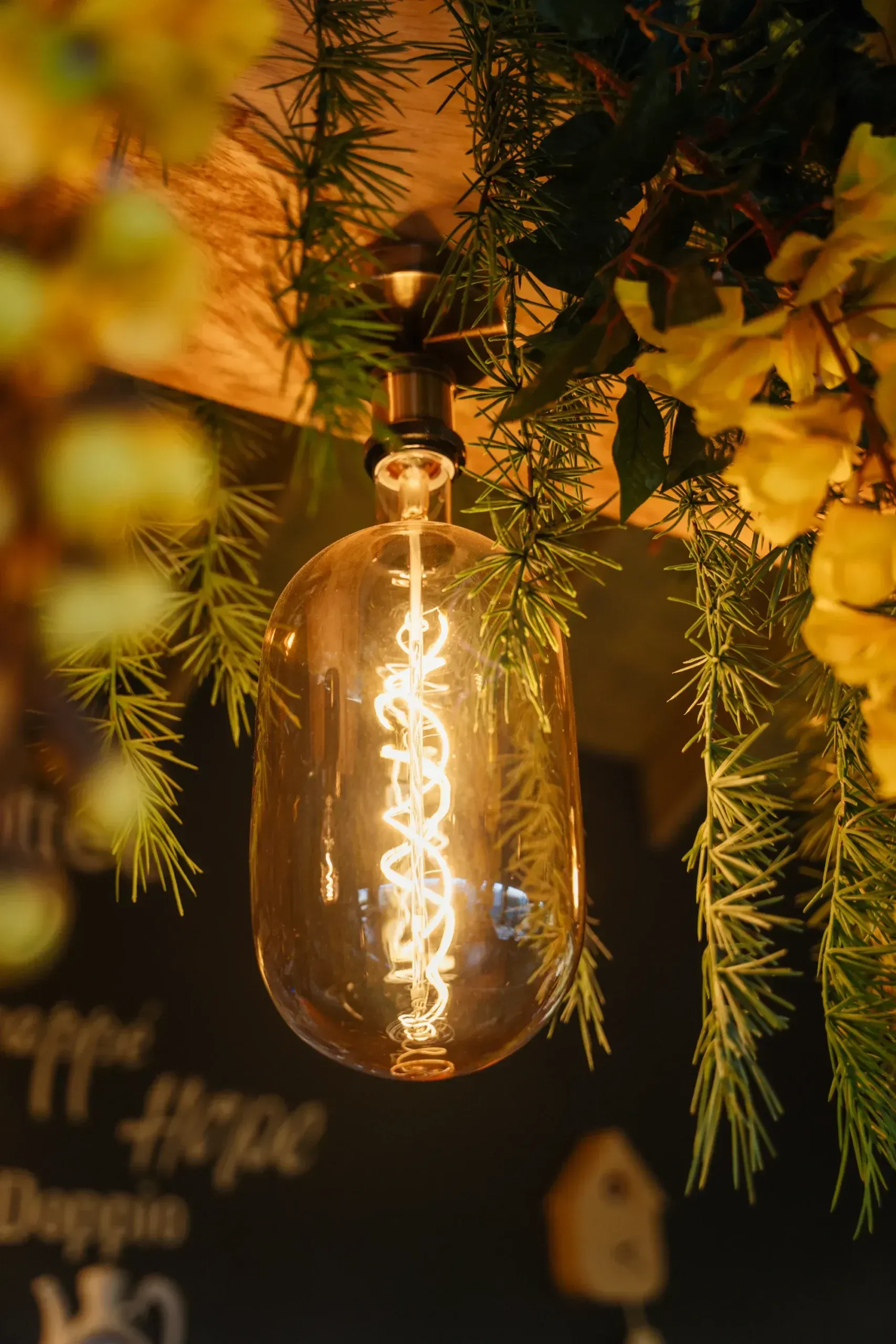 A close up of a light bulb hanging from a ceiling surrounded by flowers.