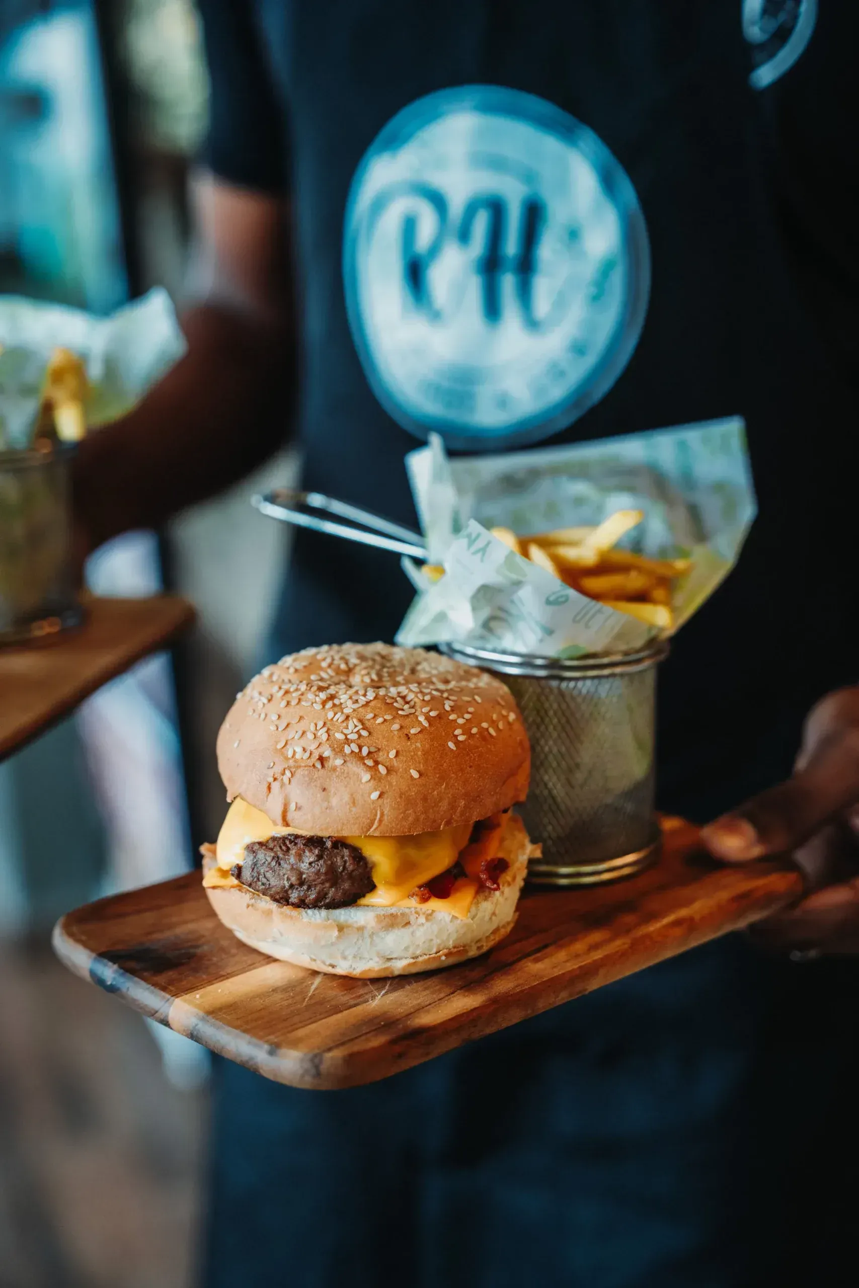 A person is holding a wooden cutting board with a hamburger and french fries on it.