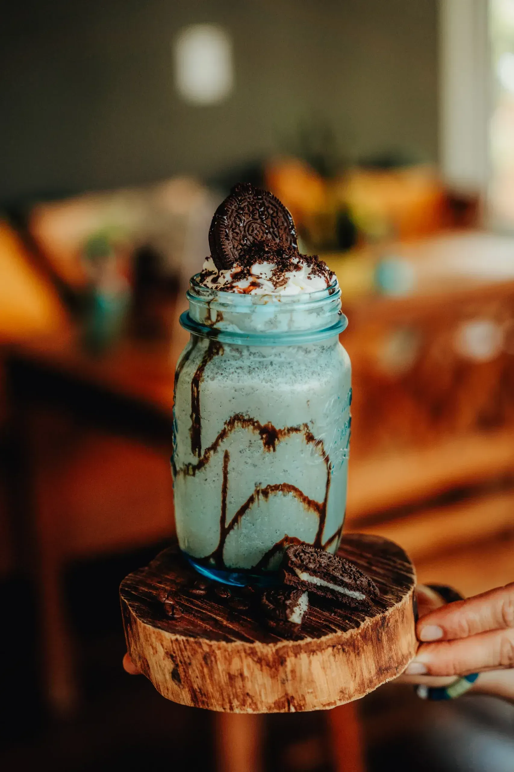 A person is holding a blue milkshake with oreos on top of it.