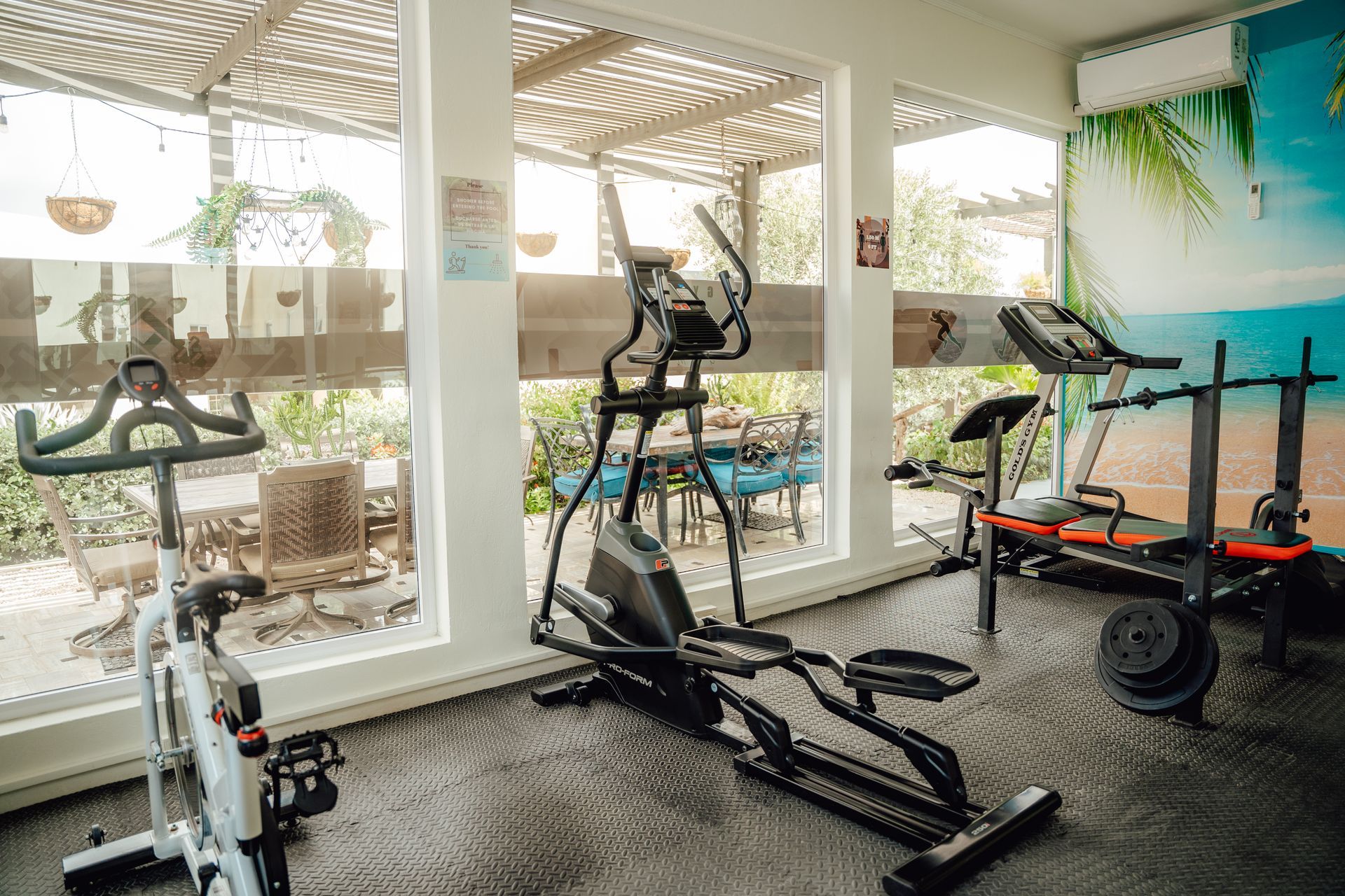 Gym with two ellipticals and a treadmill by large windows overlooking a patio