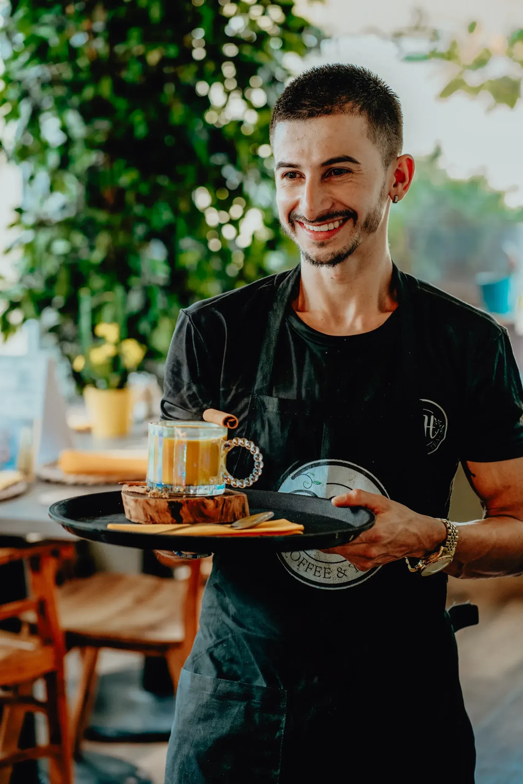 A smiling waiter is holding a tray of food in a restaurant.