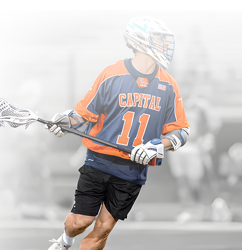A man in a capital 11 lacrosse uniform is running with a lacrosse stick.