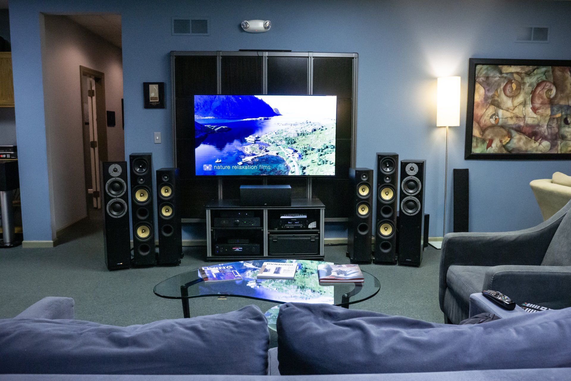 Listening room with stereo equipment, plants, artwork, and a sofa; orange walls, blue carpet.