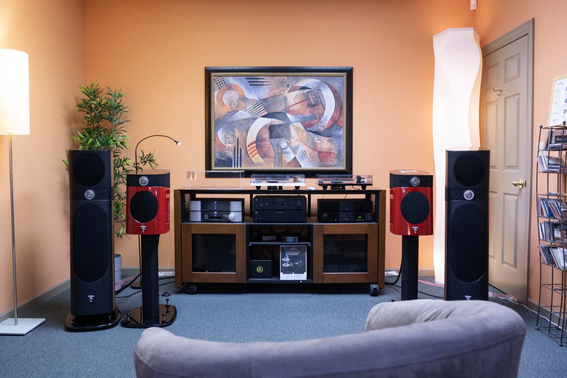 Listening room with stereo equipment, plants, artwork, and a sofa; orange walls, blue carpet.