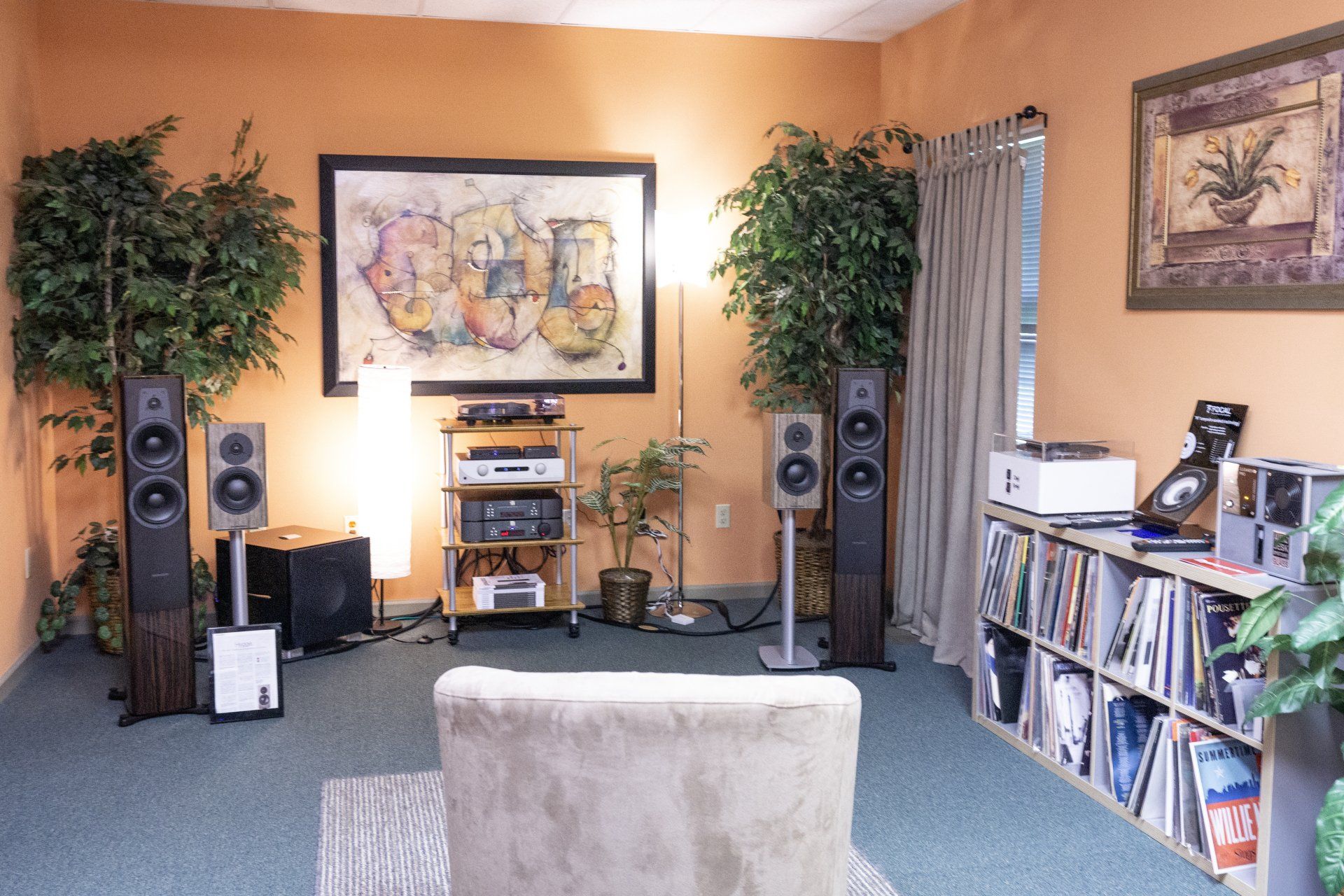 Listening room with stereo equipment, plants, artwork, and a sofa; orange walls, blue carpet.