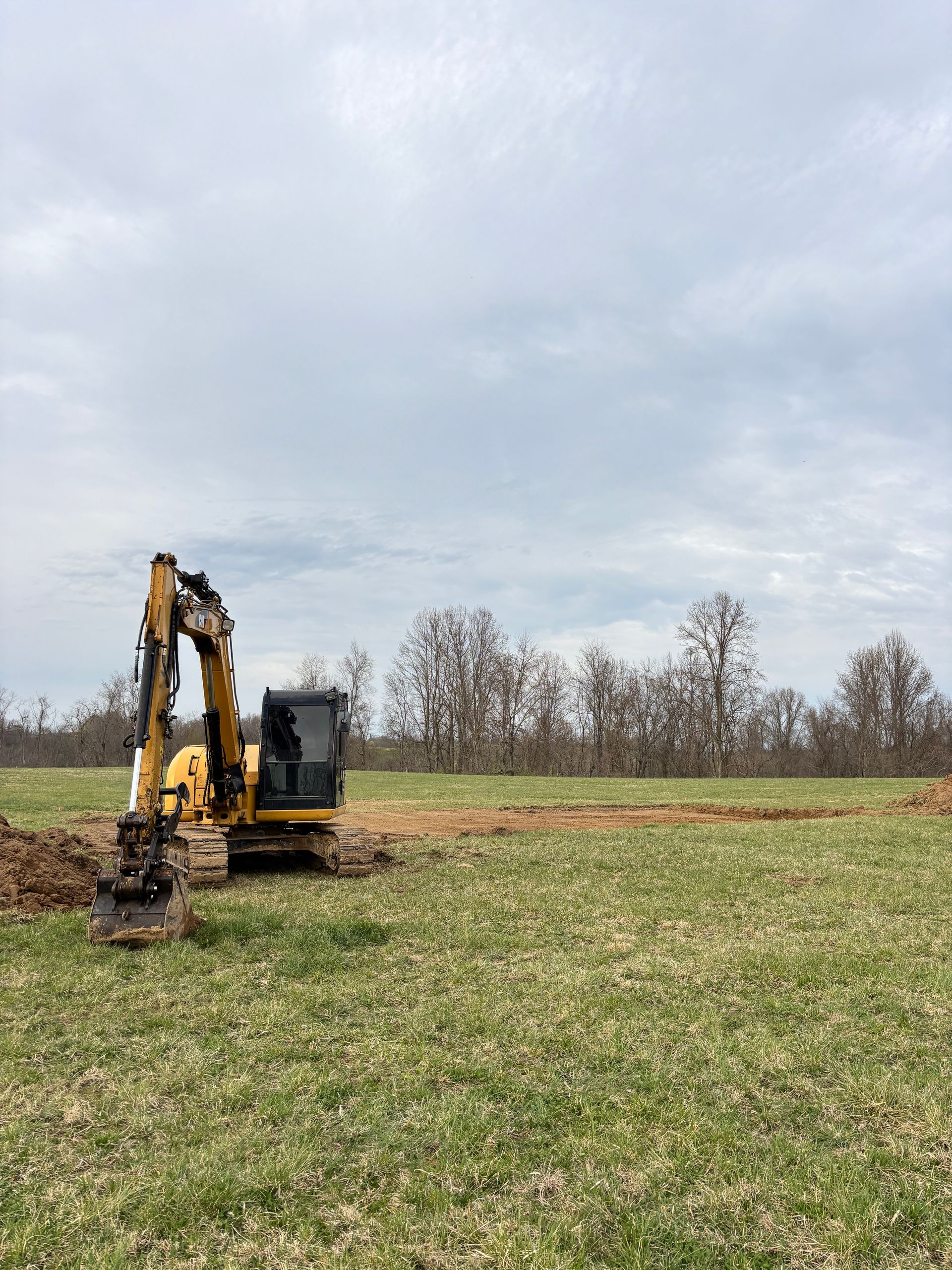Excavator bucket digging muddy soil beside a wooded roadside