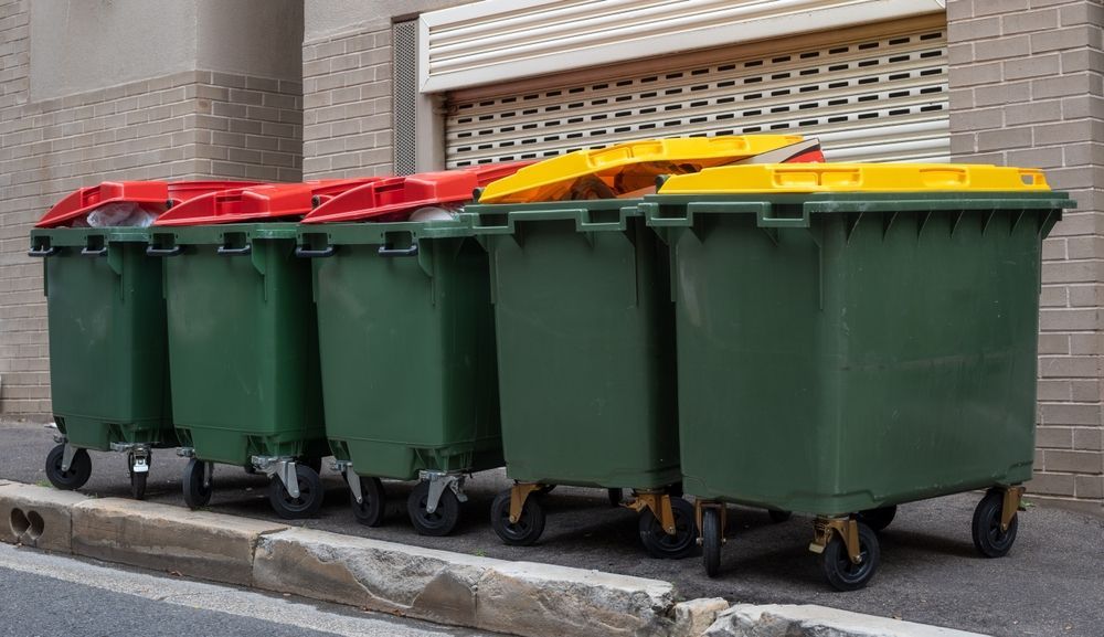 A black dumpster is sitting on top of a lush green field.
