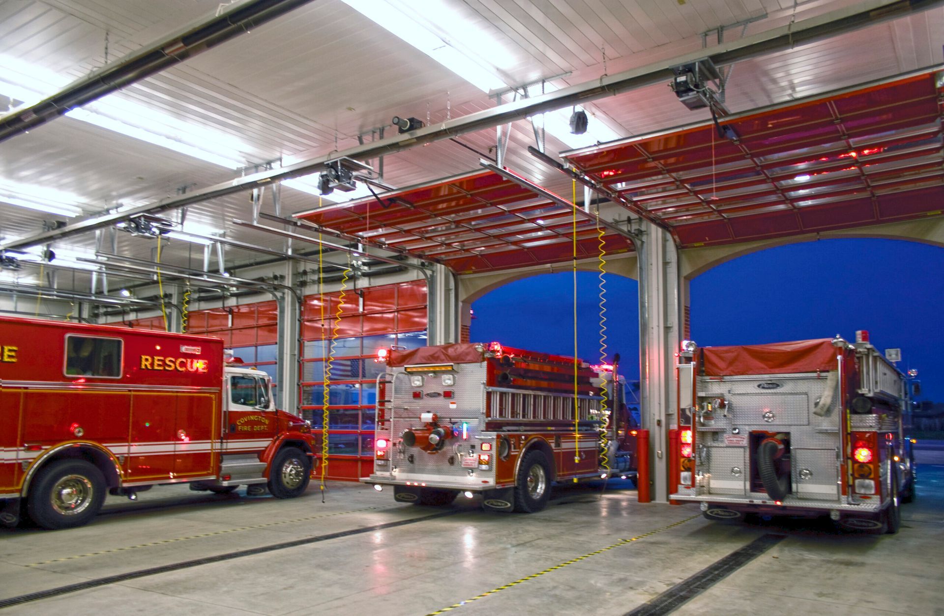 three fire trucks are parked in a fire station at night .