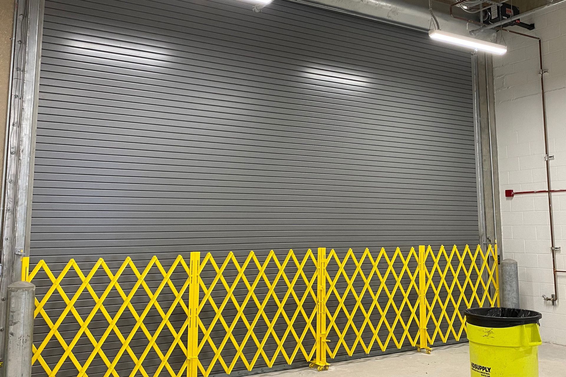 a garage door with a yellow fence around it and a yellow trash can .