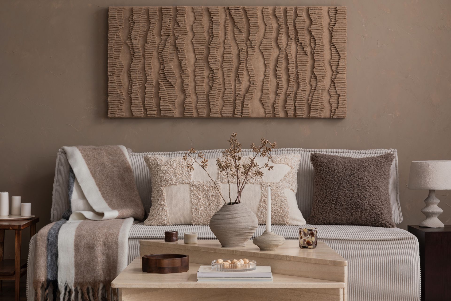 Soggiorno dai toni neutri: opere d'arte, cuscini, coperte, candele e un tavolino da caffè in legno.