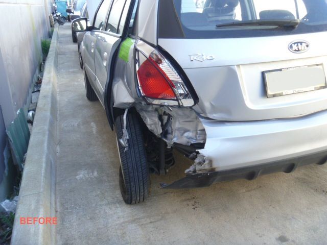 A silver car with a damaged bumper is parked on the side of the road