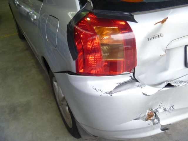 A silver car with a damaged bumper and tail light