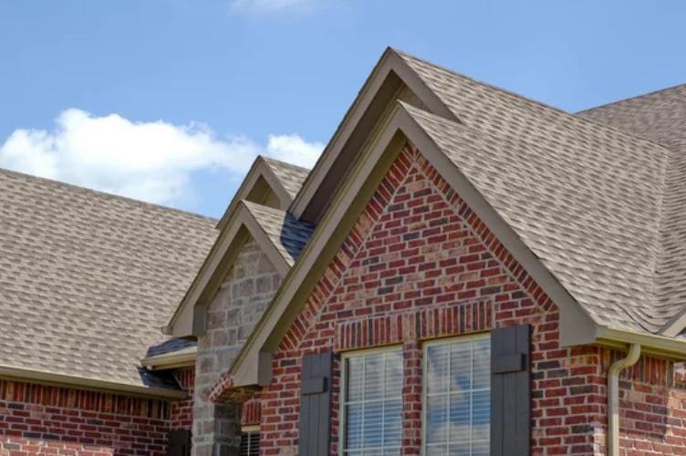 A brick house with a roof and shutters on a sunny day.