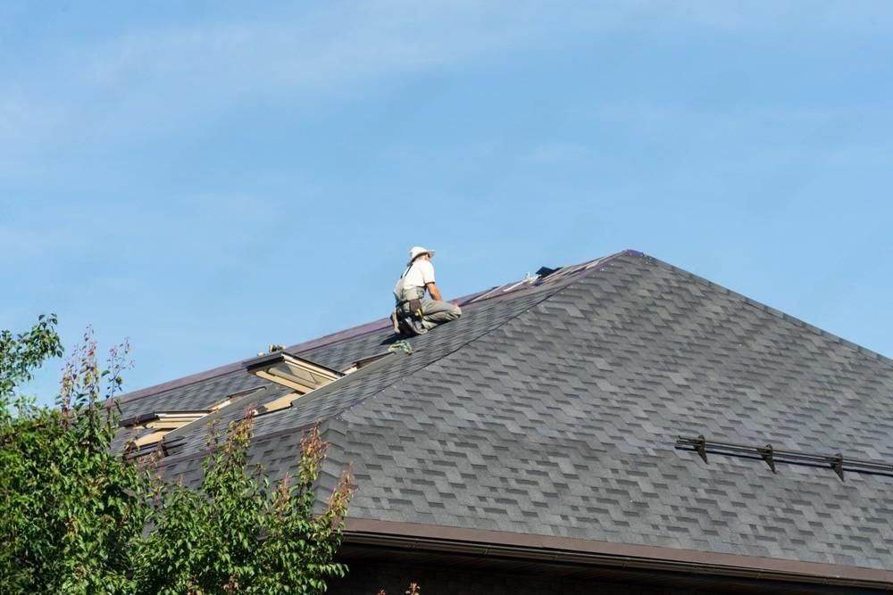 A man is sitting on the roof of a house installing asphalt roof.