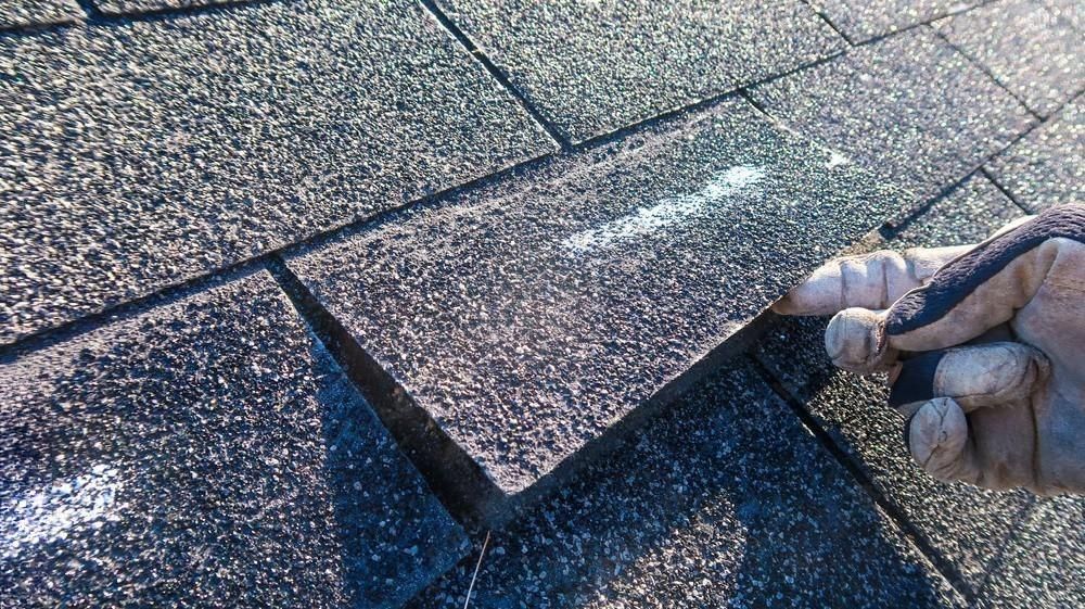 A person is holding a piece of asphalt on top of a roof.