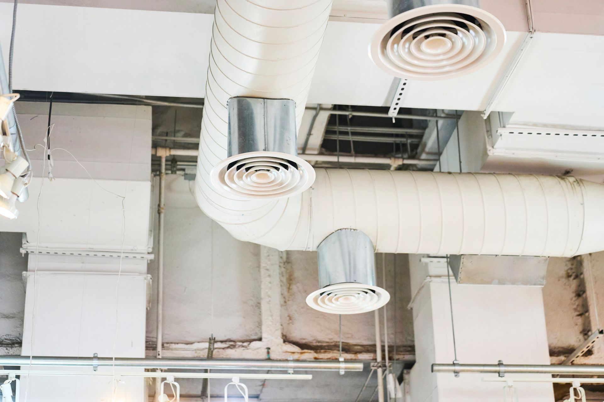 White HVAC ductwork on a ceiling, with circular and square vents.