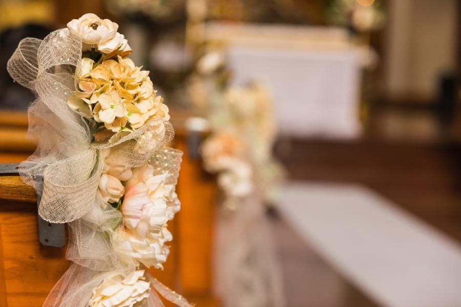 A bunch of flowers are sitting on a wooden bench in a church.