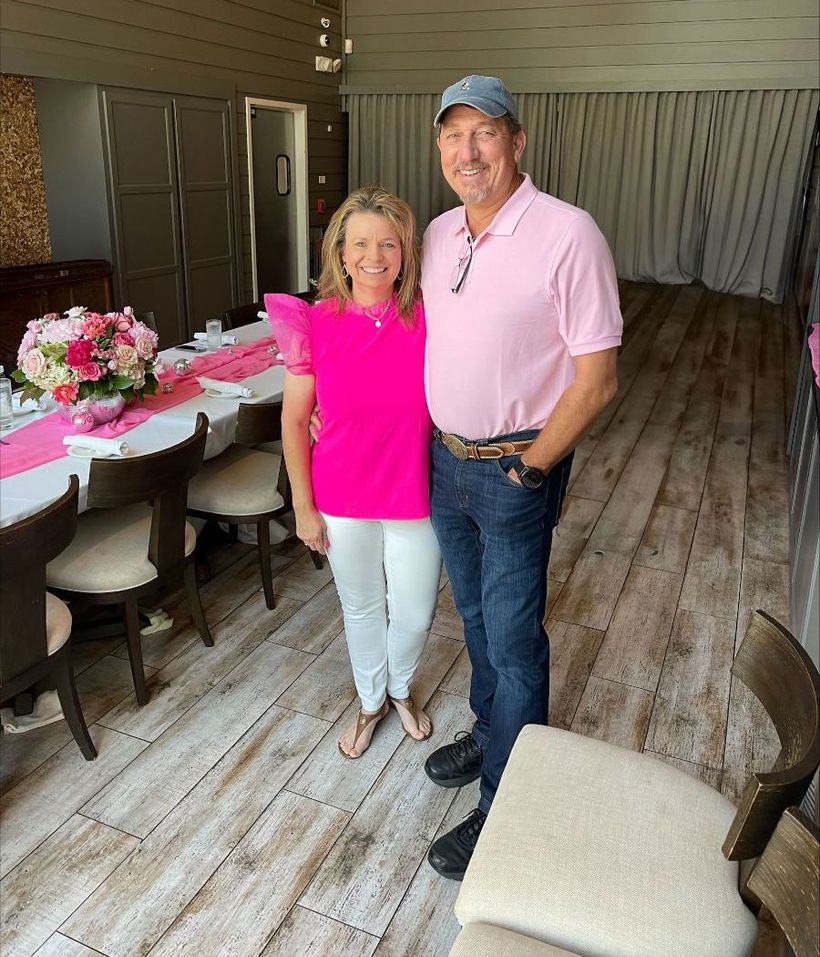 A man and a woman are posing for a picture in a room with a table and chairs.