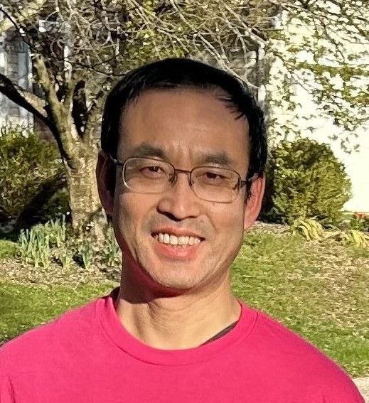 A man wearing glasses and a pink shirt is smiling for the camera.