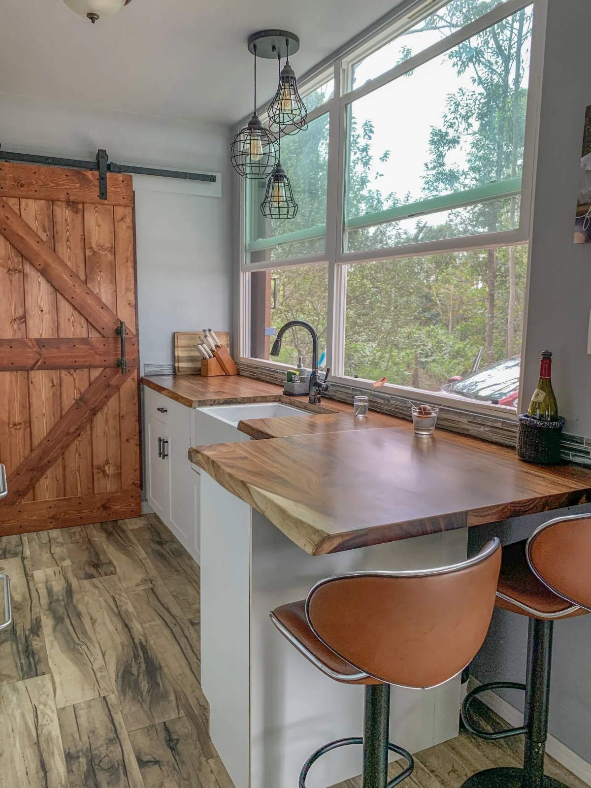 a kitchen with a wooden table , stools , a sink and a window in a shipping container home