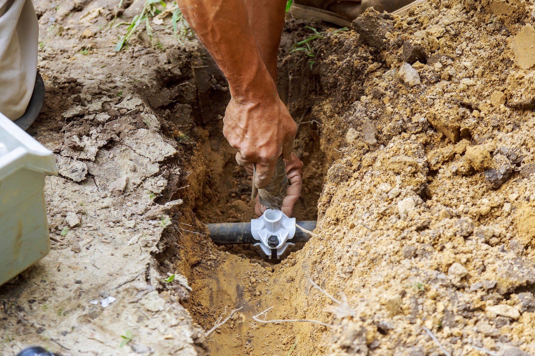 Man installing an irrigation system in a garden, carefully positioning and connecting pipes and sprinklers to ensure proper watering of plants.