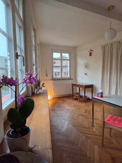 Ein farbenfrohes Wandgemälde einer Stadtszene auf einer weißen Wand, ein gelber Hocker mit Blumen und ein Türrahmen.