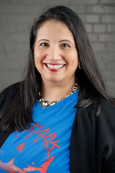 A woman wearing a blue shirt and a black sweater is smiling for the camera.