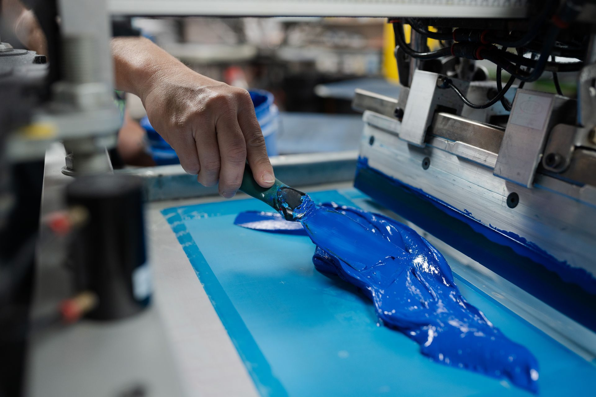 A person is applying blue paint to a screen printing machine.