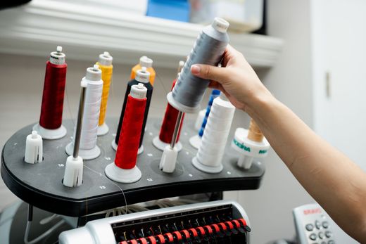 A person is holding a spool of thread in front of a machine.