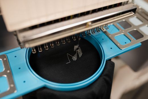 A machine is embroidery on a black shirt in a blue hoop.