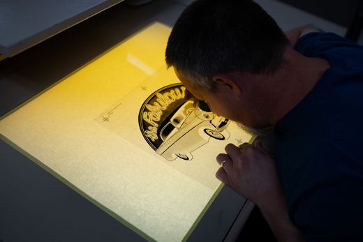 A man in a blue shirt is looking at a drawing on a light box