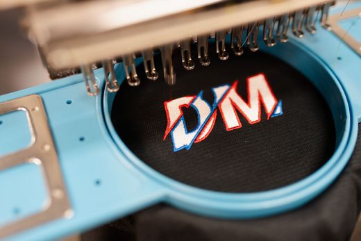 A machine is embroidery the word dym on a black cloth.