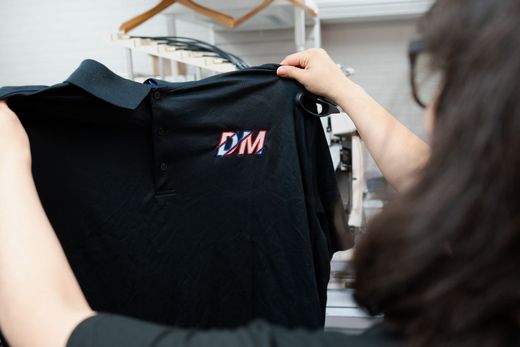 A woman is holding a black shirt with the word dm embroidered on it.