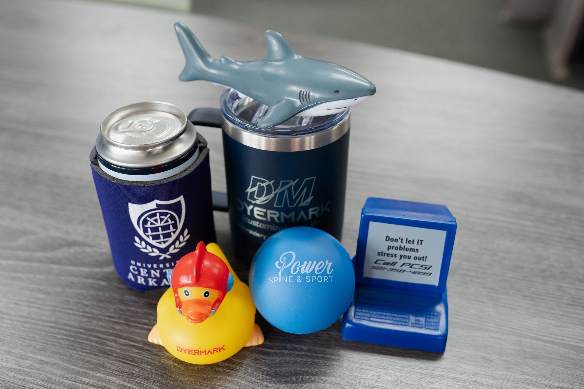 A table topped with a can of beer , a rubber duck , a ball , and a shark.