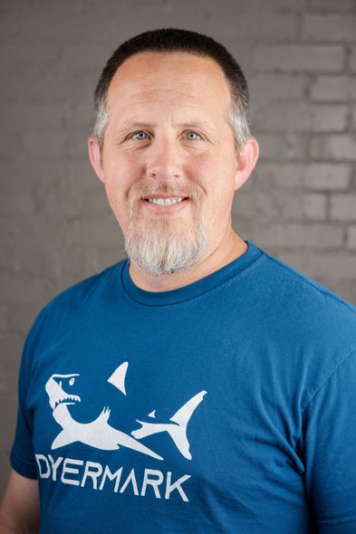 A man with a beard is wearing a blue shirt with a shark on it.