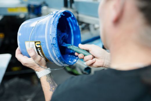 A man is holding a bucket of blue paint and a brush.