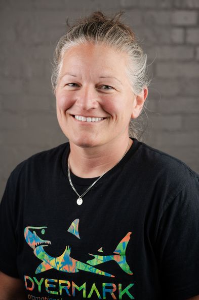 A woman wearing a black t-shirt with a shark on it is smiling for the camera.