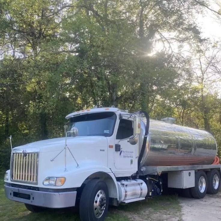 A white semi truck is parked in a grassy area with trees in the background.