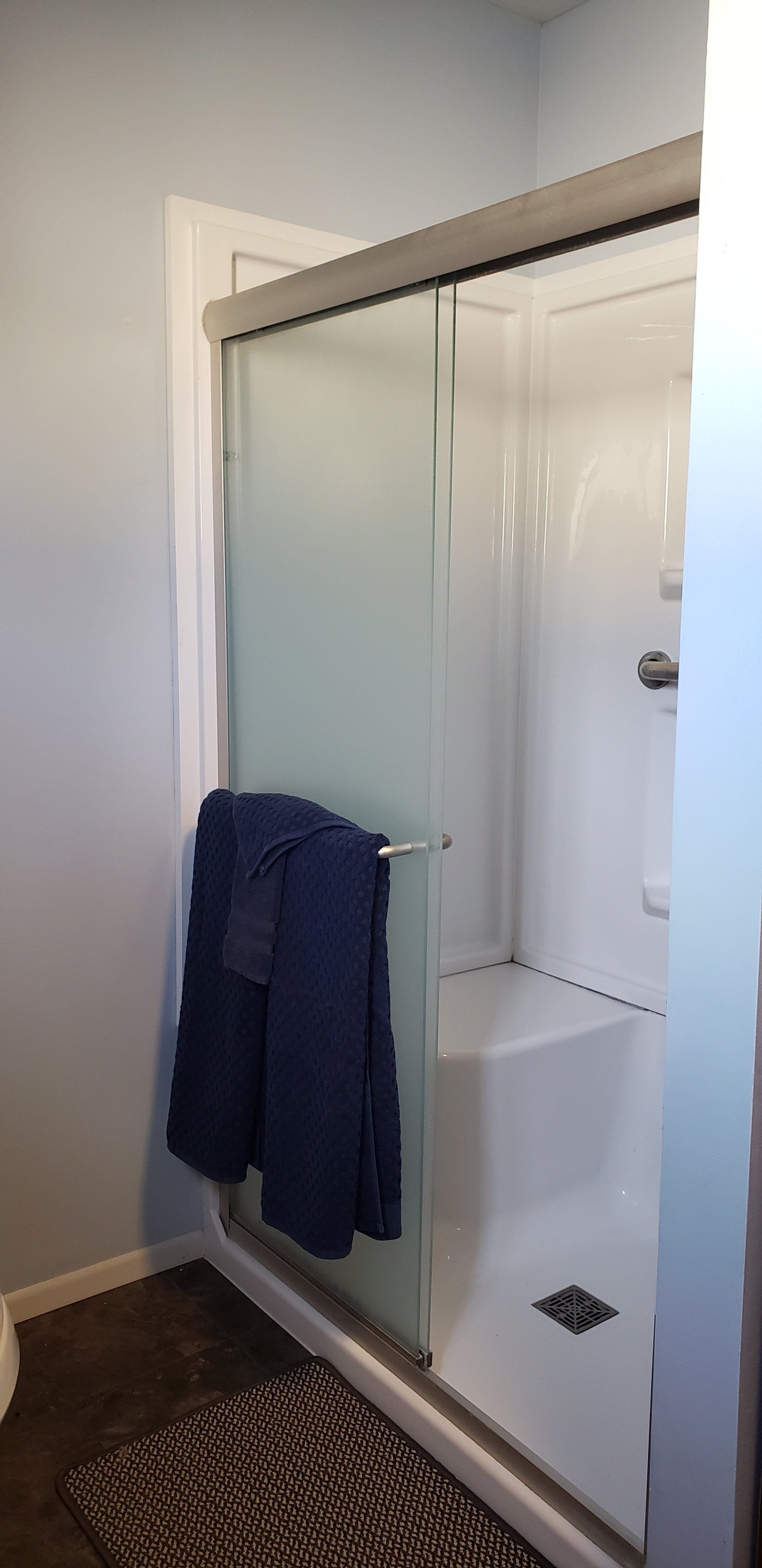 A modern bathroom with a white shower, glass door, and a dark blue towel hanging on the door handle.