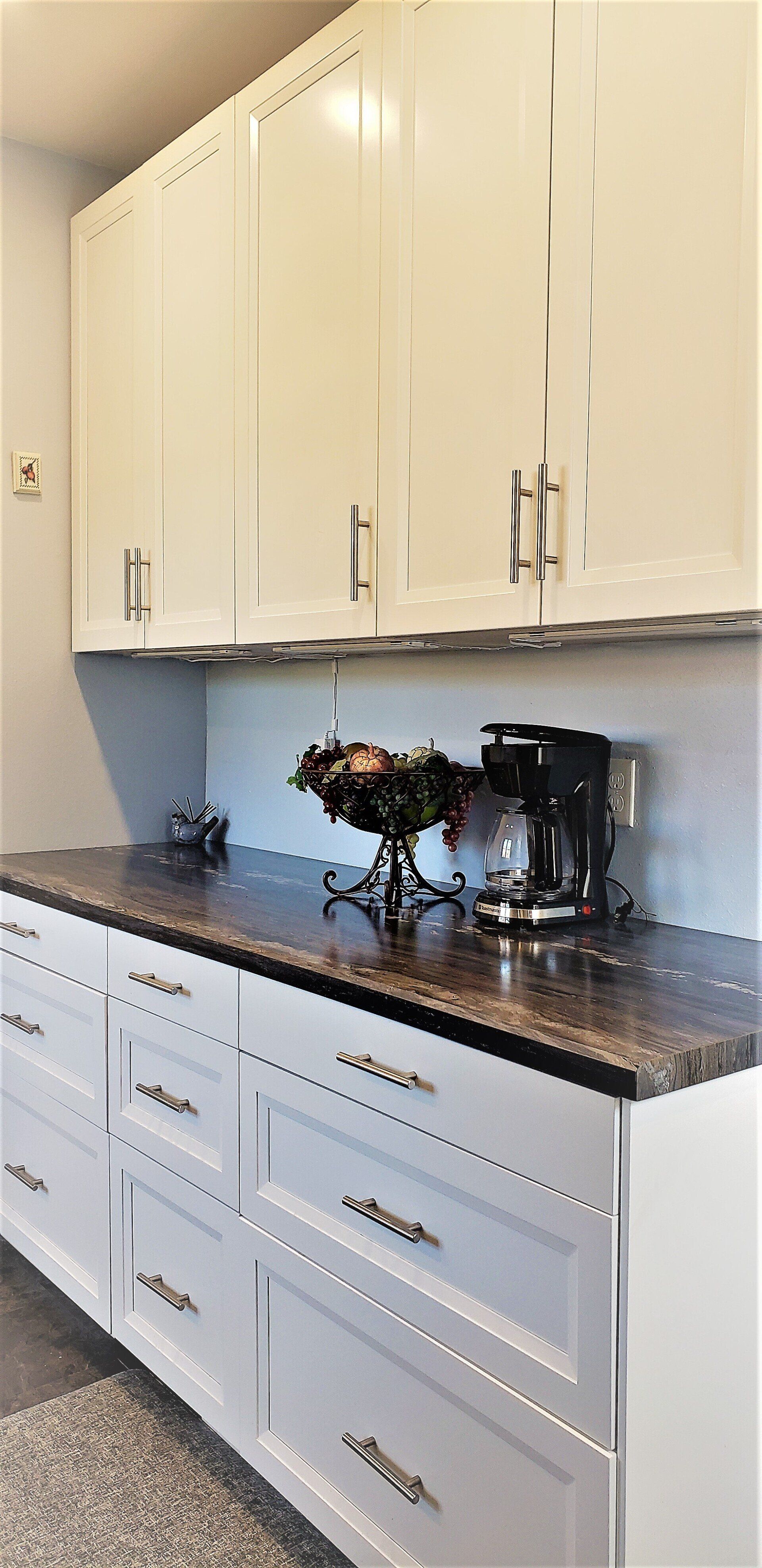 White kitchen cabinets with brown countertop, coffee maker, and fruit bowl.