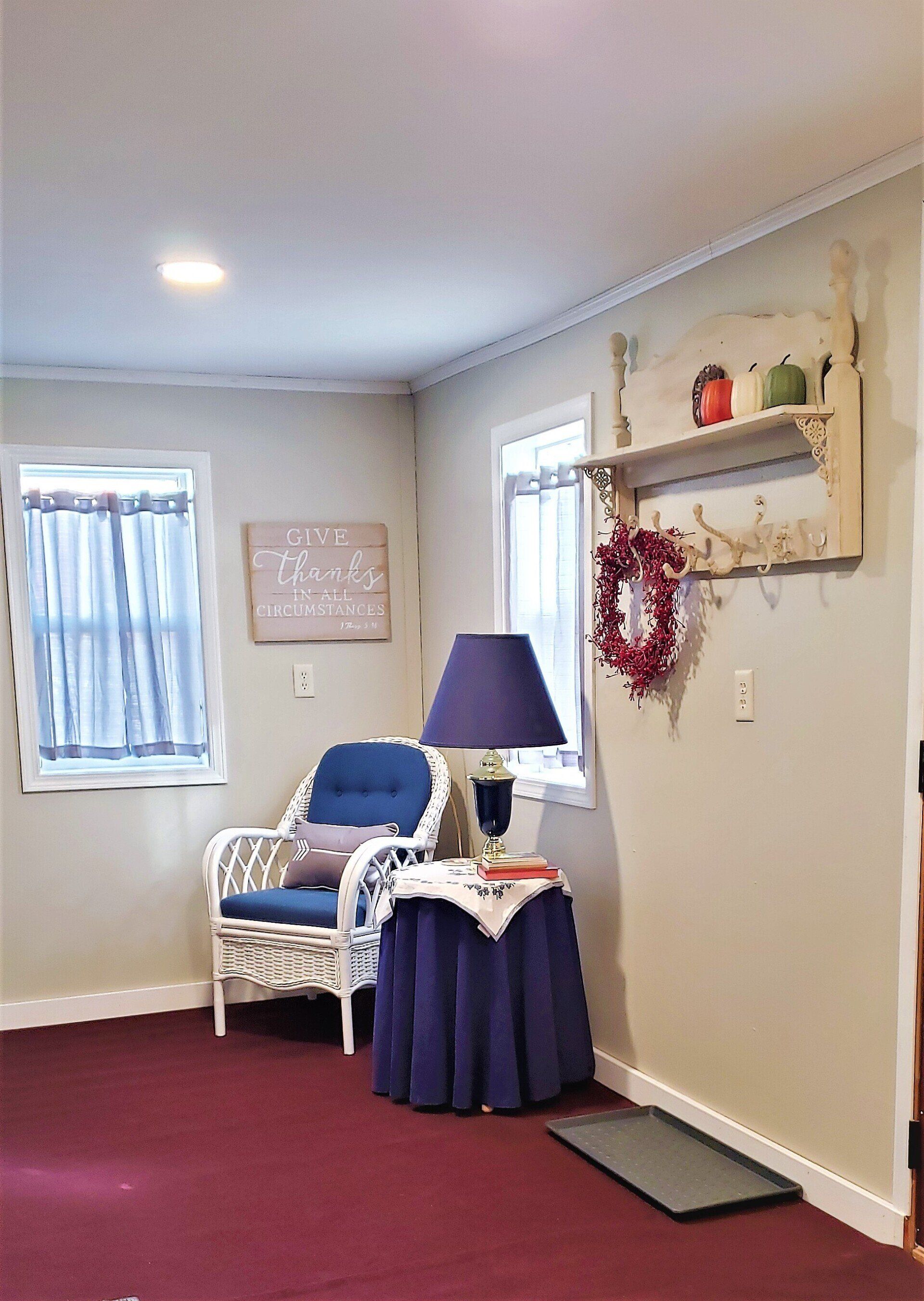 Cozy room with white wicker chair, purple lamp, small table with a purple skirt, and red rug.