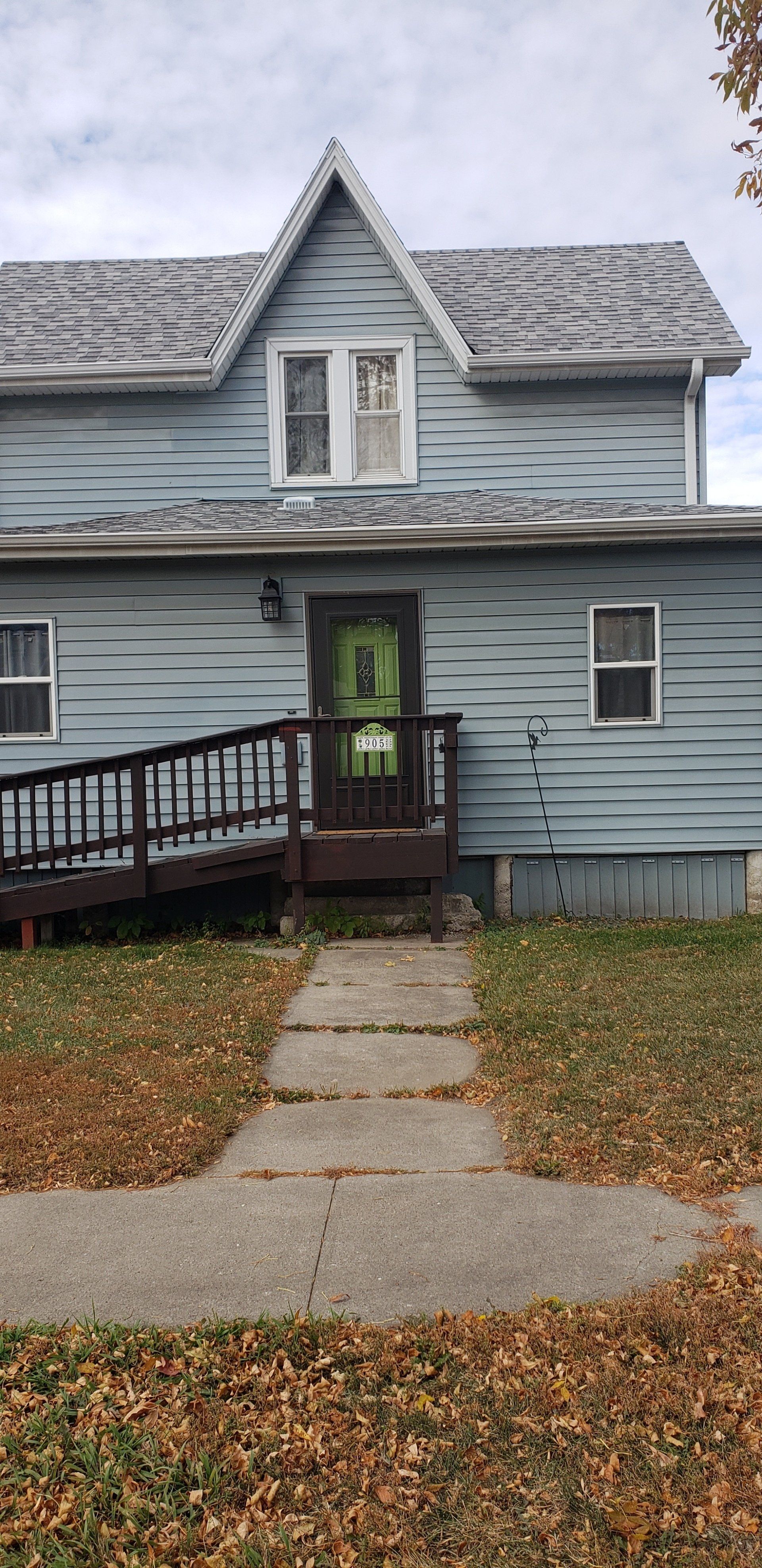 Blue house with green door and ramp, gray roof, autumn leaves.